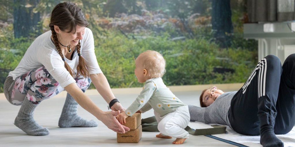 Kuopion kansalaisopisto, ilmoittautuminen ja opiskelu. Kaksi aikuista ja vauvaikäinen lapsi. Toinen aikuisista makaa lattialla ja toinen leikkii lapsen kanssa.