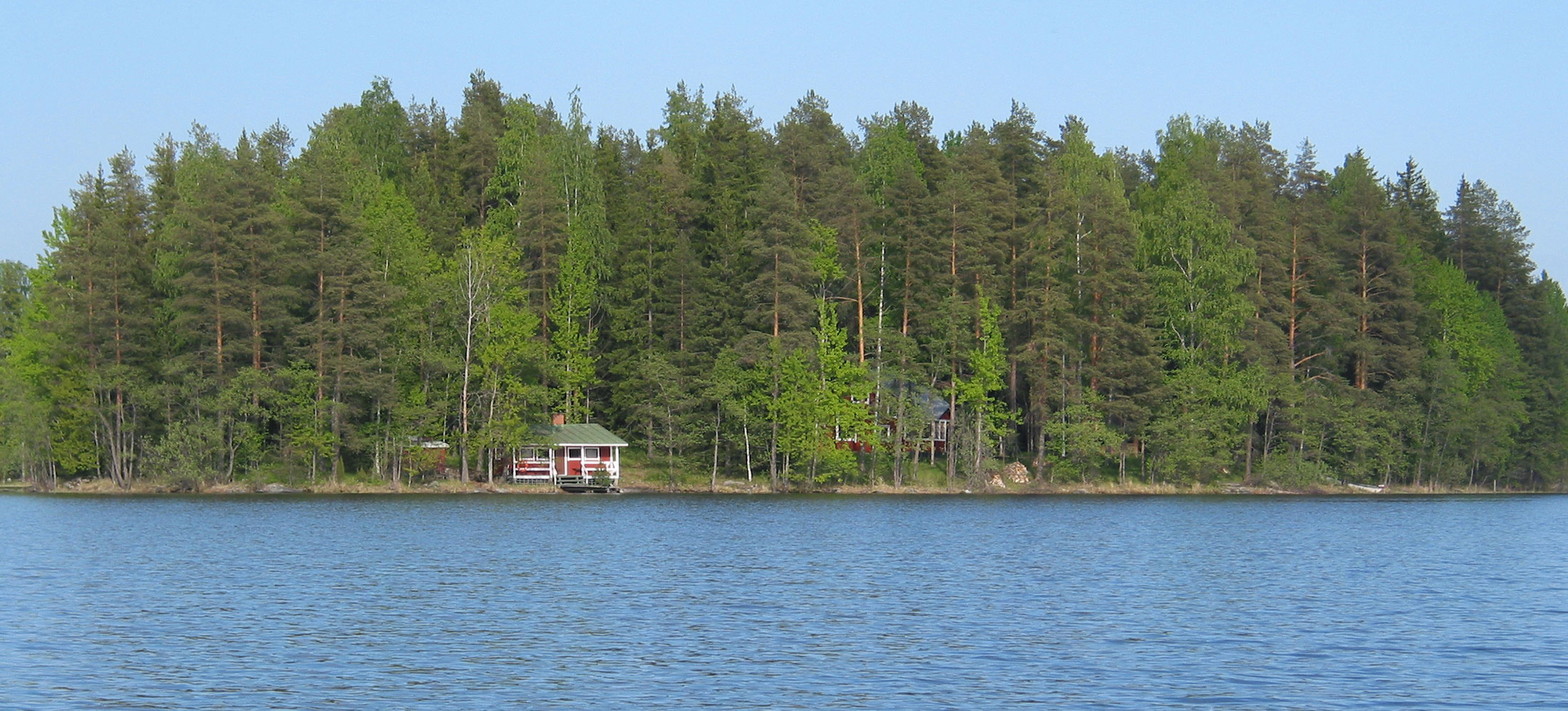 Järvimaisema, jossa saaressa punainen saunamökki
