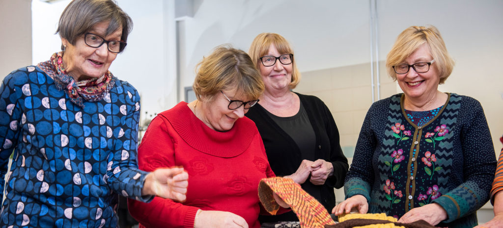 Kuopion kansalaisopisto, neljä varttunutta naista osallistumassa senioreille suunnattuun käsityökurssiin. He tutkivat tehtyjä käsitöitä.